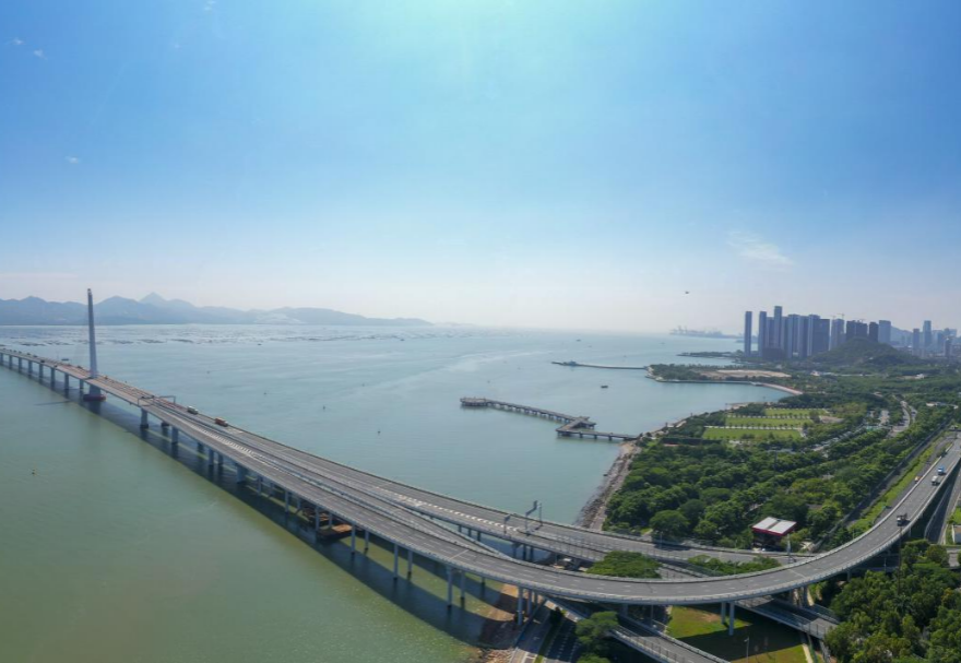 深圳灣大橋是繼羅湖、皇崗和沙頭角之后深圳第4條跨境通道，全長5545米，設(shè)南北兩個通航橋，主跨分別為210米和180米。大橋連接深圳蛇口與香港元朗，為中國公路干線網(wǎng)中唯一與香港連接的高速公路大橋，也是廣深沿江高速公路的咽喉。廣州與香港的距離因該橋建成通車縮短至100千米。大橋深圳側(cè)獨塔斜拉橋塔采用向香港側(cè)傾斜的斜塔，與香港側(cè)斜拉橋的橋塔向深圳側(cè)傾斜互相對應(yīng)，寓意深港兩地手牽手走向一起。圖為深圳灣大橋。