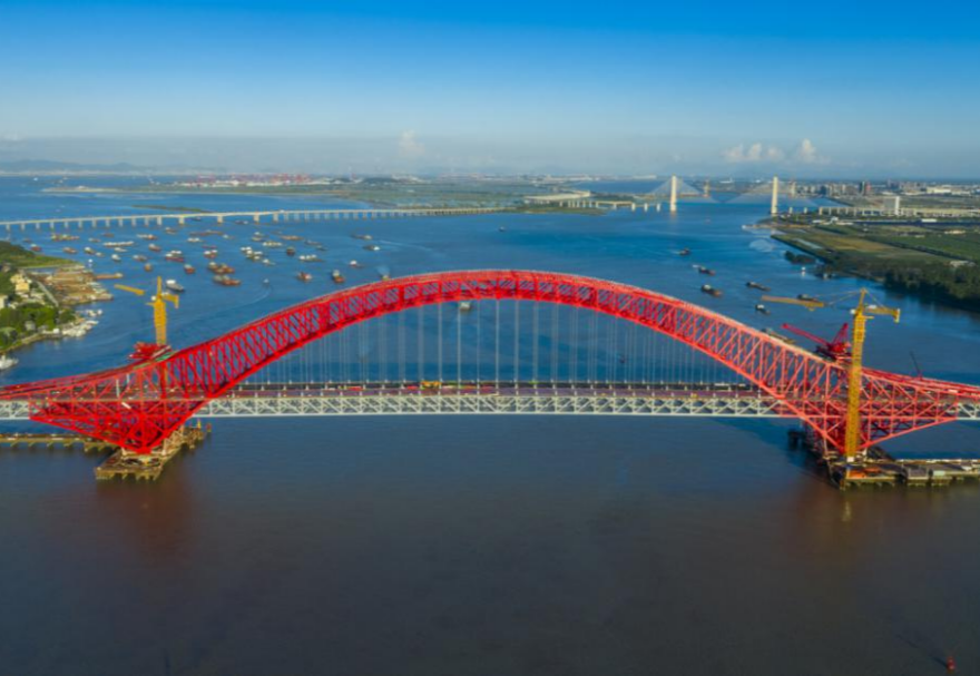 明珠灣大橋位于廣州市南沙區(qū)龍穴南水道之上，是粵港澳大灣區(qū)的重要連接通道。大橋工程全長約10.42公里，主線全長約9.1公里，主橋采用中承式六跨連續(xù)鋼桁拱橋，全長1016米，為同類型橋梁最大跨度。氣勢恢宏的明珠灣大橋綿延伸向遠方，將南沙多條核心主干道緊緊連在一起，構(gòu)筑了明珠灣區(qū)內(nèi)部核心交通環(huán)，是廣州面向粵港澳大灣區(qū)建設(shè)的交通樞紐工程和地標(biāo)性建筑。圖為南沙明珠灣大橋。