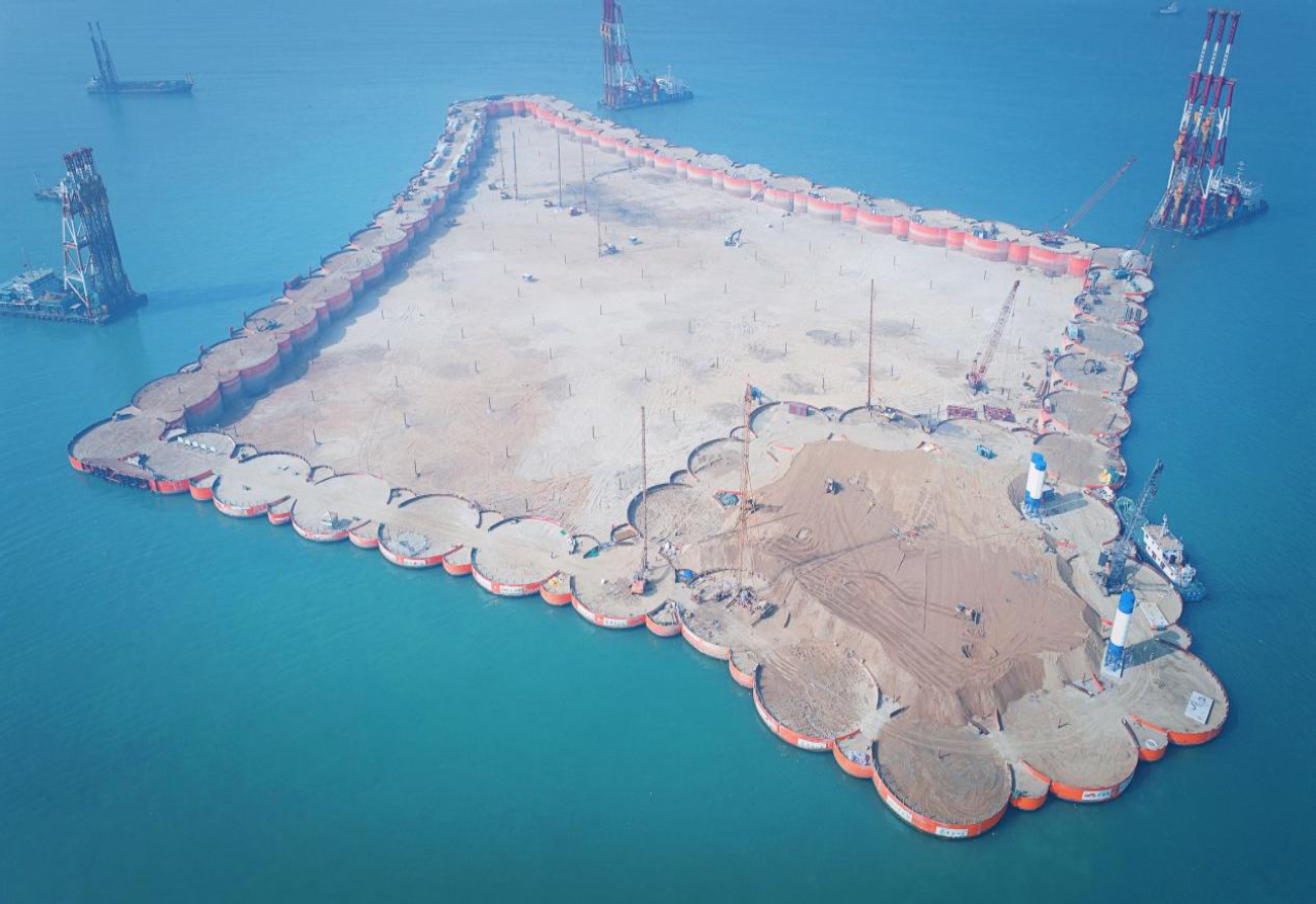 2016年12月28日，深中通道西人工島先行開建，這是深中通道工程在伶仃洋上落下的“第一子”，標(biāo)志著深中通道正式開工。西人工島島體采用菱形設(shè)計，形狀如同海上風(fēng)箏，是實現(xiàn)跨海橋梁和海底隧道轉(zhuǎn)換的關(guān)鍵。工程使用世界最大十二錘聯(lián)動液壓振動錘組，高精度振沉57個巨型鋼圓筒，歷時141天實現(xiàn)西人工島合龍，刷新了“外?？焖俪蓫u”施工紀(jì)錄。圖為深中通道西人工島海上施工現(xiàn)場。