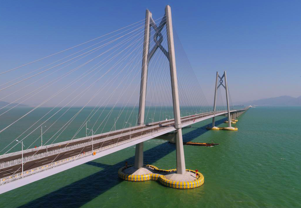 港珠澳大橋主體工程實(shí)行橋、島、隧于一體，總長約29.6公里，穿越伶仃航道和銅鼓西航道段約6.7公里為隧道，東、西兩端各設(shè)置一個(gè)海中人工島（藍(lán)海豚島和白海豚島），猶如“伶仃雙貝”熠熠生輝；其余路段約22.9公里為橋梁，分別設(shè)有寓意三地同心的“中國結(jié)”青州橋、人與自然和諧相處的“海豚塔”江海橋，以及揚(yáng)帆起航的“風(fēng)帆塔”九洲橋三座通航斜拉橋。圖為寓意三地同心的“中國結(jié)”青州橋。